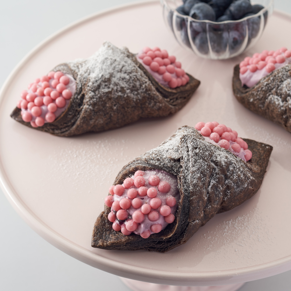 Light pastry snack made of crispy cocoa pie with blueberry cream and pink chocolate pearls filled with strawberry powder